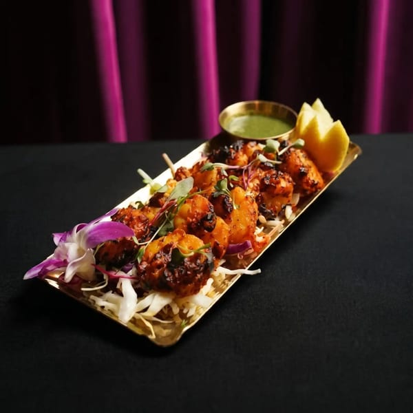 Grilled shrimp skewers with green sauce, lemon wedges, and cabbage on a golden tray.