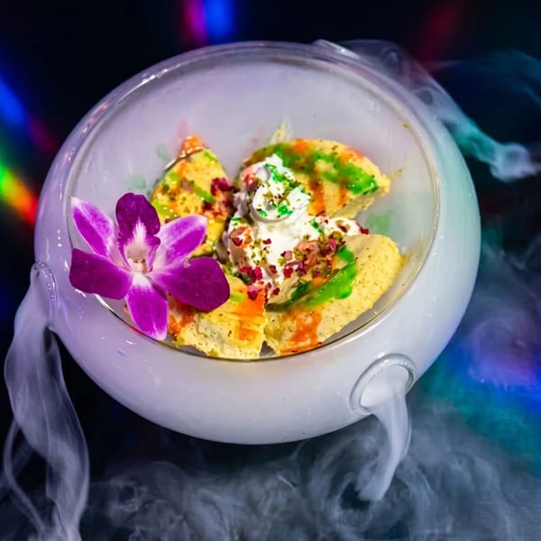Dessert in a glass bowl with dry ice smoke, topped with cream, nuts, and a purple orchid.