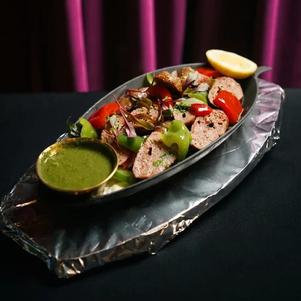 Sausage slices with red and green bell peppers, greens, a lemon wedge, and green sauce.