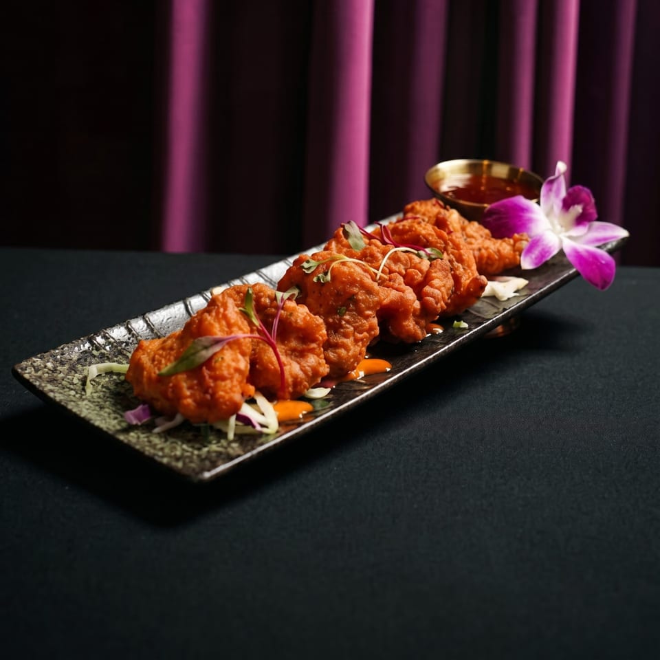 Crispy orange fried chicken pieces on a rectangular plate with sauce and an orchid.